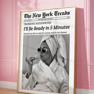 K&ouml;nnte beinhalten: Gerahmter Schwarz-Wei&szlig;-Druck einer Frau im Bademantel und Sonnenbrille, die ein Getr&auml;nk h&auml;lt. Der Druck ist ein Mock-Zeitungs-Cover mit dem Titel "The New York Trends" mit der Schlagzeile "I'll Be Ready in 5 Minutes."