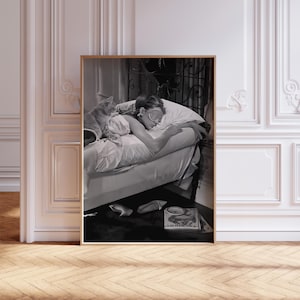May include: Black and white photo of a woman sleeping in bed with a cat. The woman is wearing a sleep mask and is lying on her side. The cat is curled up on the bed next to her. The photo is framed in a wooden frame.