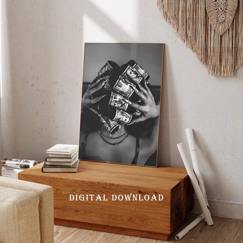 May include: Black and white framed print featuring a person holding a large bundle of US dollar bills in front of their face. The print is labeled "DIGITAL DOWNLOAD" at the bottom. The print is displayed on a wooden table.