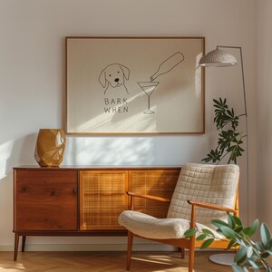 K&ouml;nnte beinhalten: Ein rechteckiger gerahmter Wandkunstdruck mit einer minimalistischen schwarzen Strichzeichnung eines Hundes und einer Flasche, die Fl&uuml;ssigkeit in ein Martiniglas gie&szlig;t, mit dem Text BARK WHEN in Schwarz auf hellbeigem Hintergrund.