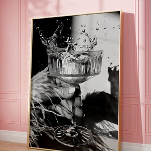 May include: A black and white photograph of a hand holding a stemmed glass with water splashing out of it.
