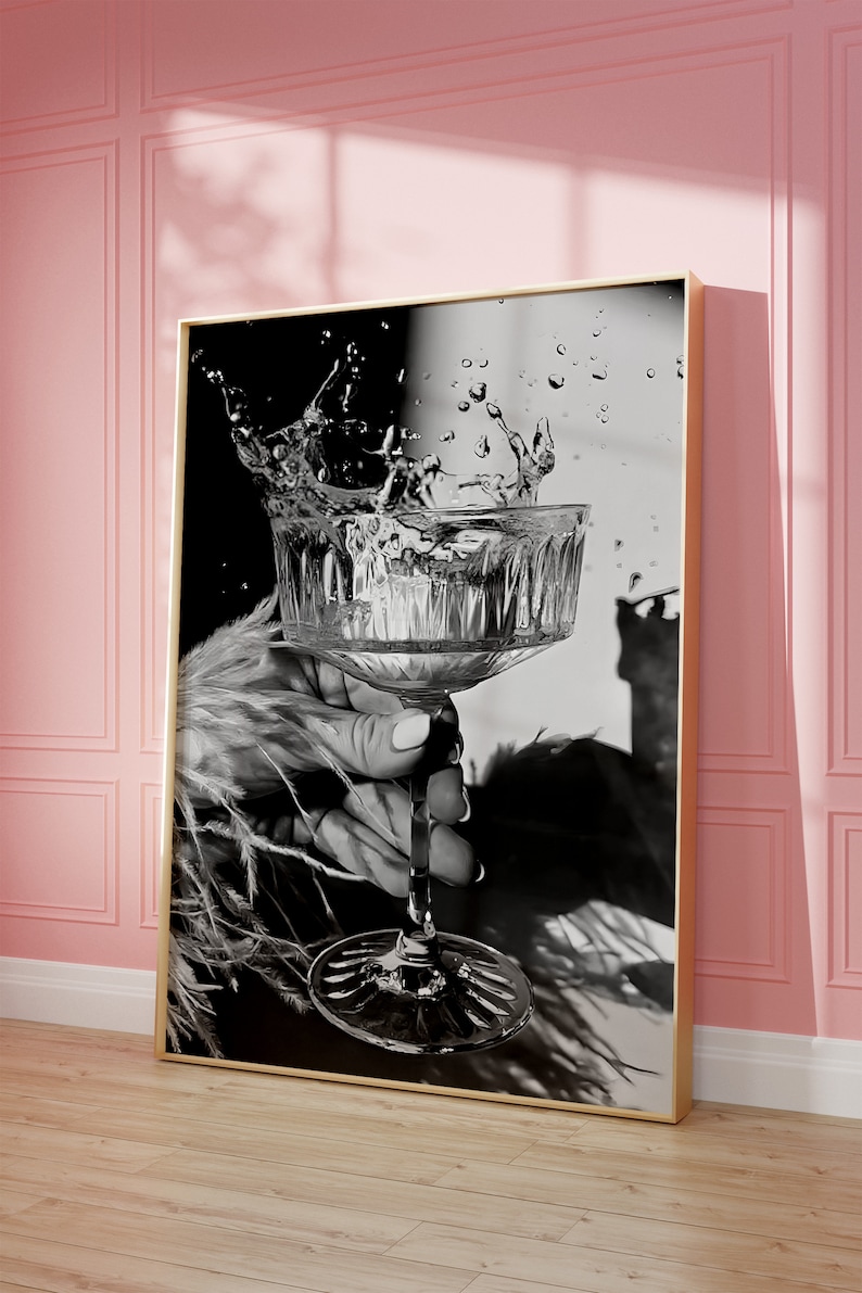 May include: A black and white photograph of a hand holding a stemmed glass with water splashing out of it.