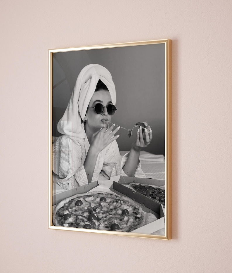 Pu&ograve; includere: Stampa in bianco e nero incorniciata di una persona con occhiali da sole e un asciugamano in testa, che mangia la pizza. Due scatole di pizza sono aperte di fronte a lei. La stampa &egrave; in una cornice dorata.