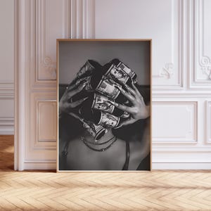 May include: Black and white framed print featuring a person with long nails holding rolled-up US dollar bills. The person is wearing a necklace and a dark top. The image is a close-up shot.