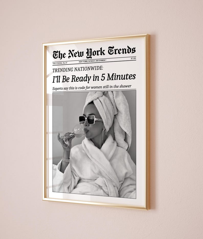 K&ouml;nnte beinhalten: Gerahmter Druck mit goldenem Rahmen. Der Druck ist eine gef&auml;lschte Zeitung, "The New York Trends", mit der Schlagzeile "I'll Be Ready in 5 Minutes". Das Bild ist ein Schwarz-Wei&szlig;-Foto einer Frau in Bademantel und Sonnenbrille.