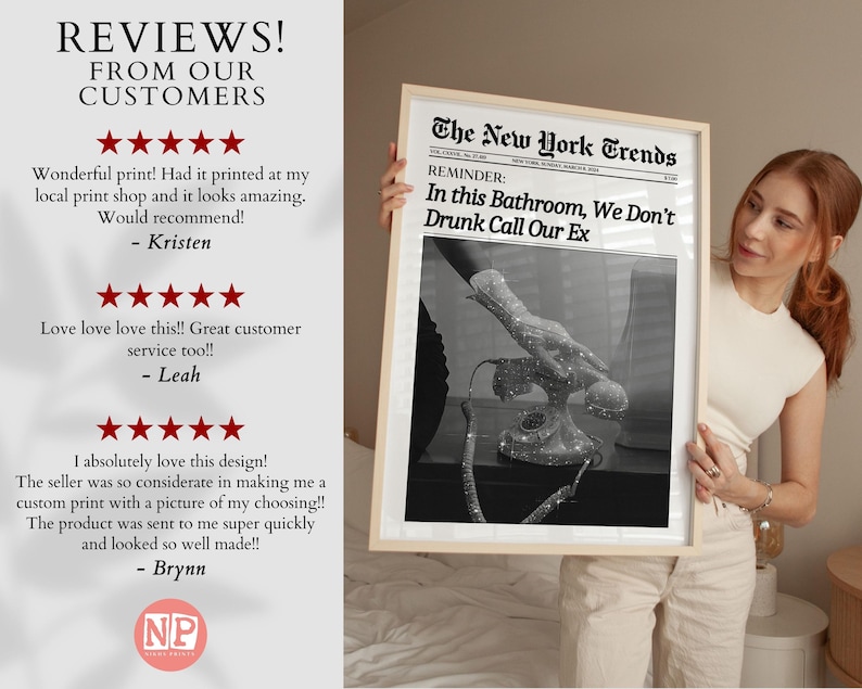 May include: A framed black and white print with the text "The New York Trends" and "In this Bathroom, We Don't Drunk Call Our Ex". The print features a vintage rotary phone with a hand reaching towards it. The print is held by a person wearing a white top and beige trousers.