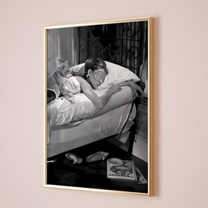 May include: A black and white photograph of a woman sleeping in bed with a cat. The woman is wearing a sleep mask and has her arm around the cat. The cat is curled up on the bed next to the woman. The photo is framed in a gold frame.