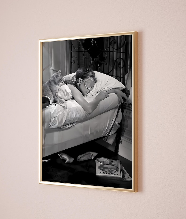 May include: A black and white photograph of a woman sleeping in bed with a cat. The woman is wearing a sleep mask and has her arm around the cat. The cat is curled up on the bed next to the woman. The photo is framed in a gold frame.