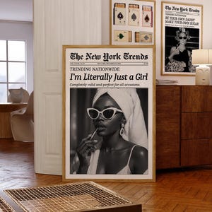 May include: A room interior featuring framed art prints. The main print is a black and white image of a person applying lipstick, with the text "I'm Literally Just a Girl." Other prints include playing card designs and a newspaper-style print with the text "BE YOUR OWN DADDY MAKE YOUR OWN SUGAR."