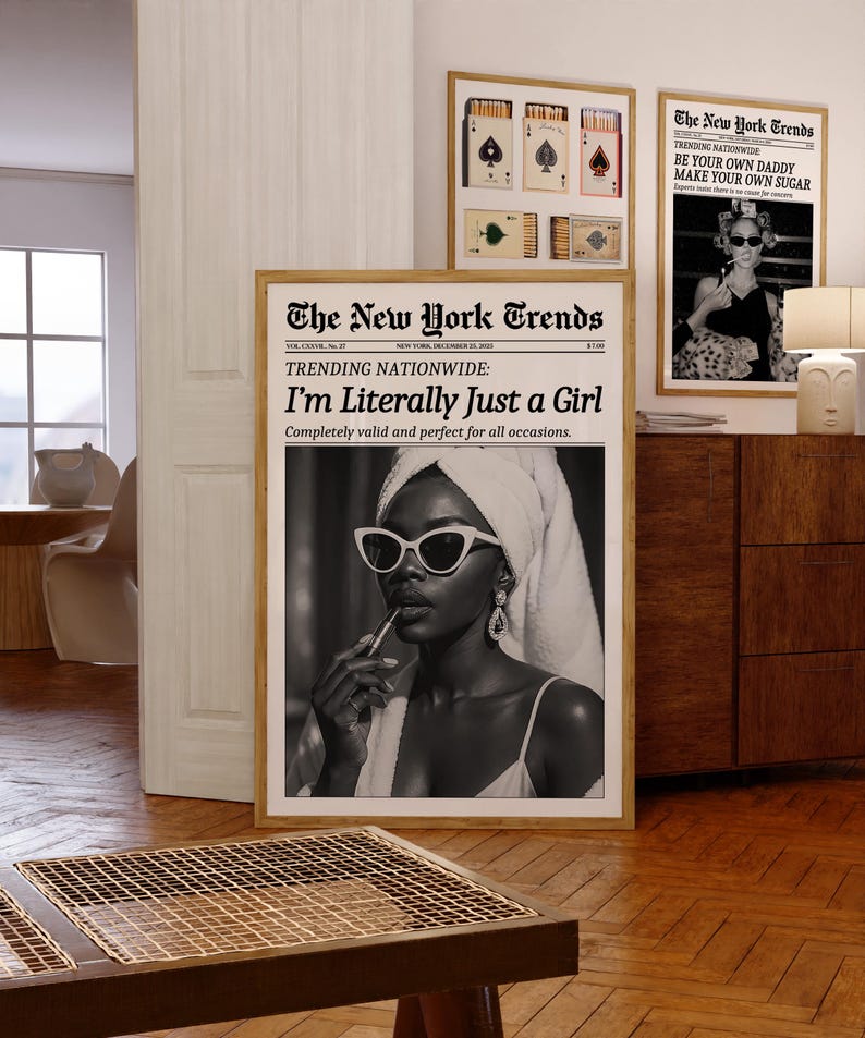 May include: A room interior featuring framed art prints. The main print is a black and white image of a person applying lipstick, with the text "I'm Literally Just a Girl." Other prints include playing card designs and a newspaper-style print with the text "BE YOUR OWN DADDY MAKE YOUR OWN SUGAR."