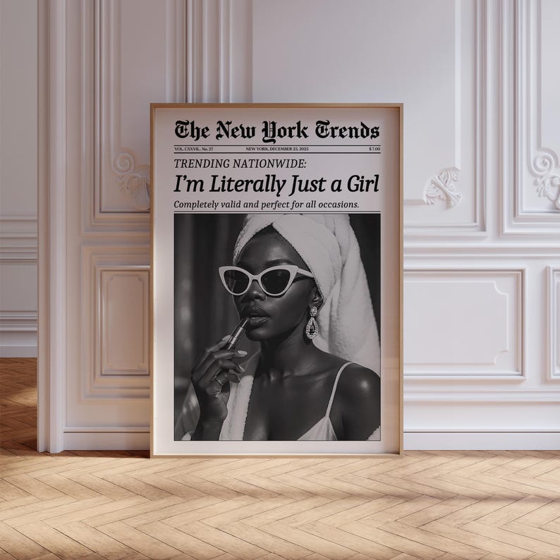 May include: A framed black and white print featuring a woman wearing sunglasses and a towel on her head, applying lipstick. The print is designed to look like a newspaper, with the headline "The New York Trends" and the text "I'm Literally Just a Girl."