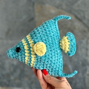 May include: A crocheted blue and yellow fish toy. The fish has a yellow stripe around its body and a yellow fin. The fish has a black eye.