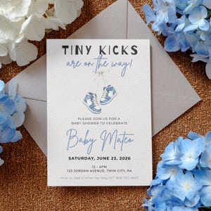 Könnte beinhalten: Eine weiße Babyparty-Einladungskarte mit dem Text TINY KICKS are on the way! und einer Illustration von zwei hellblauen und weißen Turnschuhen, die mit Schnürsenkeln verbunden sind. Die Karte enthält Details für Baby Mateo am 23. Juni 2026.