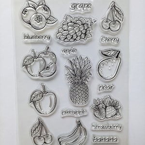 Op de afbeelding: Een doorzichtig siliconen stempelvel met zwarte lijntekeningen van diverse vruchten, waaronder bosbessen, druiven, kersen, appels, een ananas, een peer, aardbeien en bananen, voorzien van de bijbehorende namen in een sierlijk lettertype.