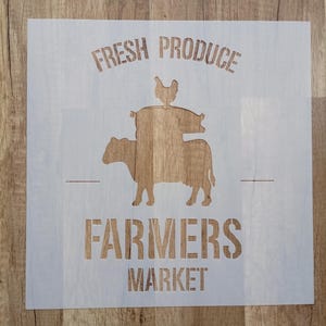 Könnte beinhalten: Eine quadratische, halbtransparente Schablone mit dem Text FRESH PRODUCE oben und FARMERS MARKET unten. In der Mitte zeigt eine gestapelte Silhouettengrafik ein Huhn, das auf einem Schwein sitzt, welches auf einer Kuh steht.