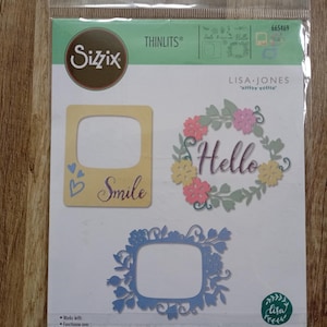 Può includere: Set di fustelle Sizzix Thinlits di Lisa Jones, con tre design decorativi: una cornice gialla con "Smile", una ghirlanda floreale con "Hello" e una cornice floreale blu. La confezione include 15 fustelle.