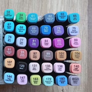 Op de afbeelding: Een verzameling van zesendertig rechthoekige markers gerangschikt in een raster. Elke markerdop toont een uniek nummer en kleurnaam, waaronder tinten zoals Mint Green Light, Prussian Blue, Vivid Purple, Natural Oak en Warm Grey, onder andere.