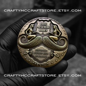 May include: A bronze-colored coin with the text "FREE MUSTACHE RIDES" and "PRIVATELY OWNED AND OPERATED". The coin features two mermaid figures and a stylized mustache design. The text "OPEN 24/7" is also visible. The Etsy shop name is displayed.