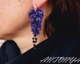 May include: Purple flower earrings with a silver hook and a dangling chain of purple beads. The earrings are in the shape of a cluster of flowers.