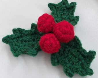 May include: A handmade crochet holly sprig with three red berries. The leaves are a deep green, and the berries are a vibrant red. This festive decoration is perfect for adding a touch of holiday cheer to any craft project or home decor.