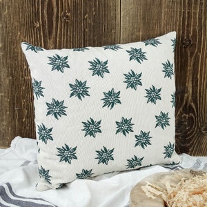 May include: A white cushion with a green floral pattern. The cushion is made of a soft, comfortable fabric and features a repeating pattern of green edelweiss flowers.