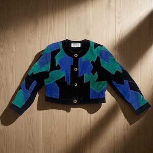 May include: A cropped jacket featuring a geometric color-block pattern in black, royal blue, and emerald green. The garment has a round neckline, long sleeves, and a front button closure with four circular buttons. A label reading DINO Z is visible.