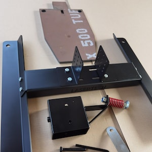Könnte beinhalten: Ein schwarzer Metallständer mit einer roten Feder und einer kleinen schwarzen Box. Der Ständer trägt ein Etikett mit der Aufschrift "LASERTECH". Es gibt auch mehrere Schrauben, Muttern und einen Schraubenschlüssel.