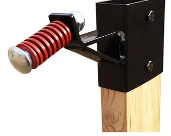 May include: Black metal gate latch with a red spring-loaded handle attached to a wooden post. The latch is designed to secure a gate.