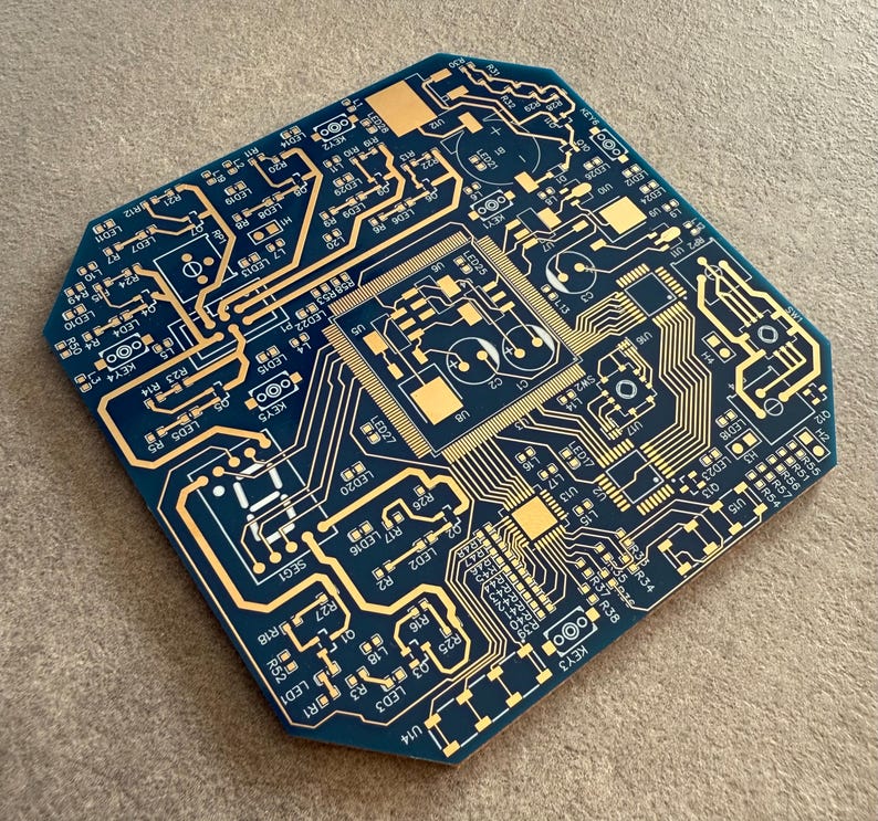 May include: A blue and gold circuit board featuring detailed electronic pathways and components. The board has a distinctive, geometric shape and is designed with a complex network of lines and symbols, showcasing a technological theme.