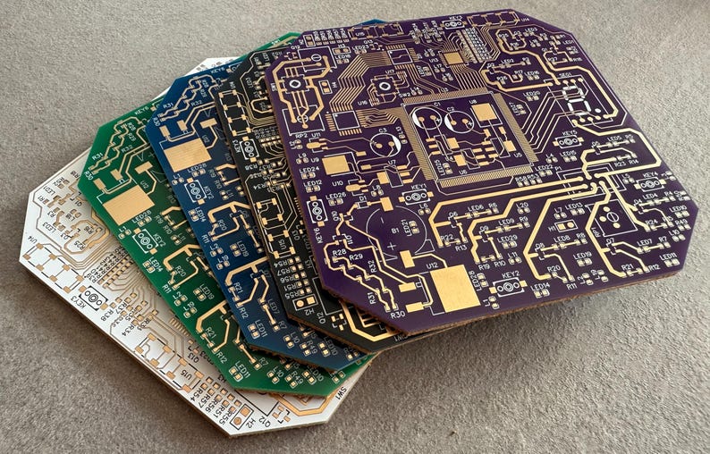 May include: A stack of colourful circuit boards with intricate gold-coloured traces and components. The boards are in shades of white, green, blue, and purple. The boards have a unique octagonal shape.