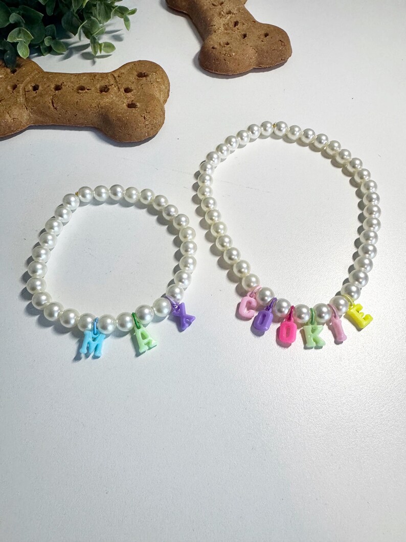 May include: Two pearl necklaces with colourful letter charms spelling out the names "Max" and "Cookie".