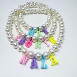 May include: A white pearl necklace with colourful letter charms spelling out the name "Naomi".