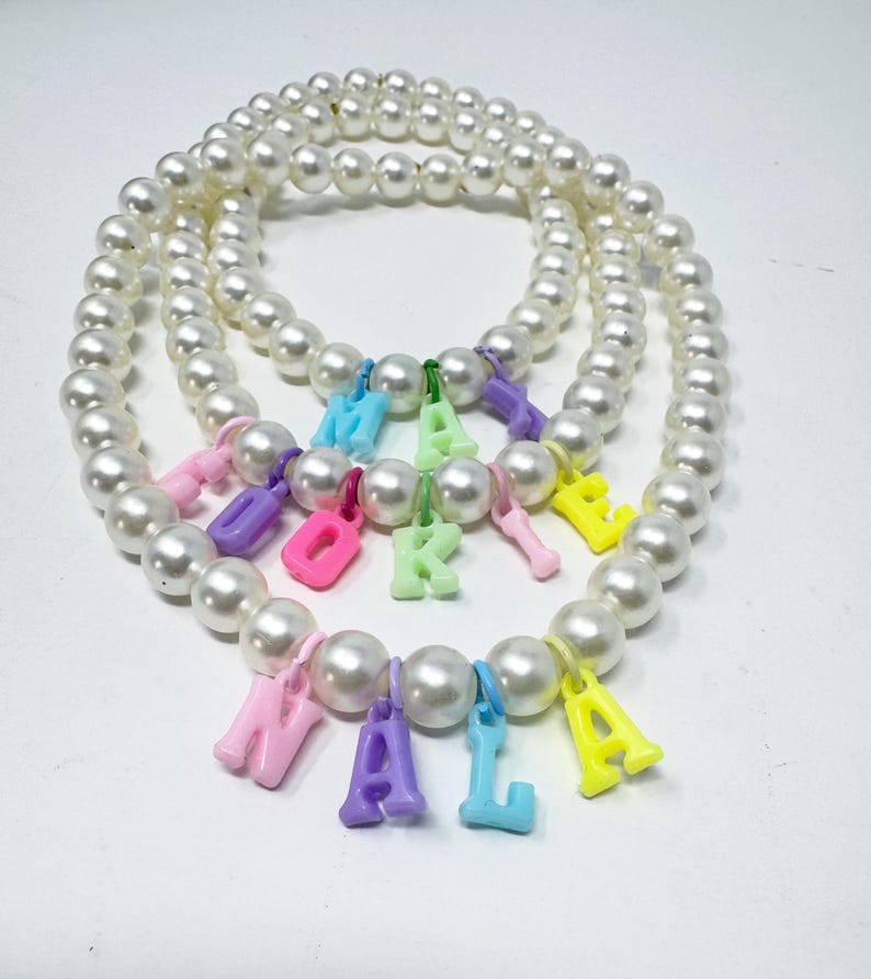 May include: A white pearl necklace with colourful letter charms spelling out the name "Naomi".