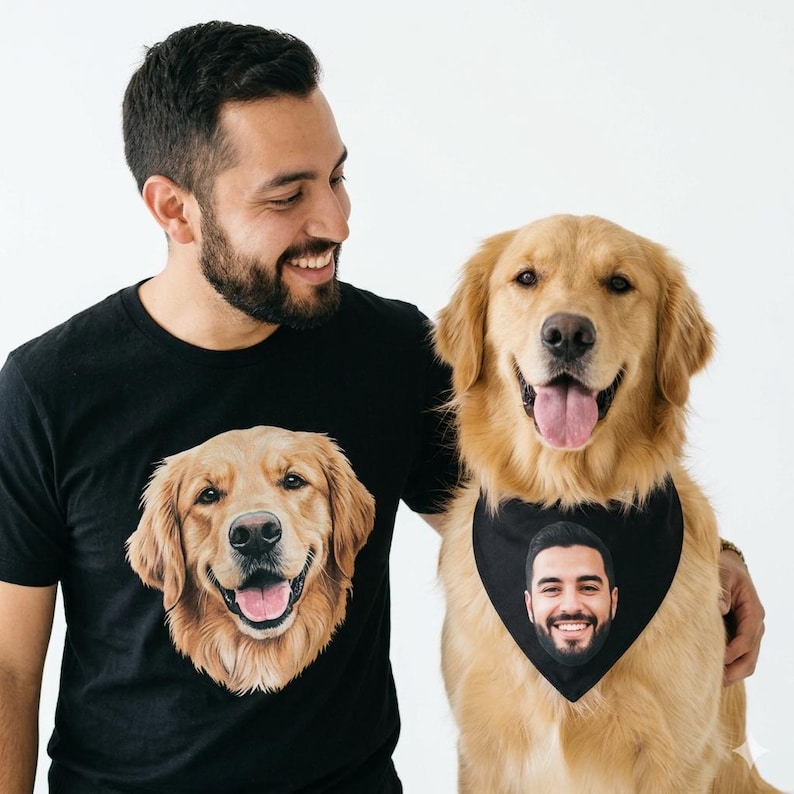Op de afbeelding: Een zwart t-shirt met een afdruk van het gezicht van een golden retriever. Een golden retriever draagt een zwarte bandana met een afdruk van het gezicht van een persoon. De persoon lacht en kijkt naar de hond.