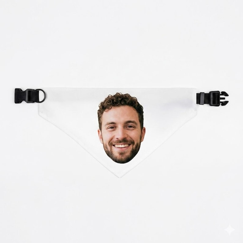 Op de afbeelding: Witte driehoekige bandana voor huisdieren met een afdruk van het gezicht van een lachende man. De bandana heeft zwarte plastic verstelbare gespen aan elk uiteinde. De achtergrond is effen wit.