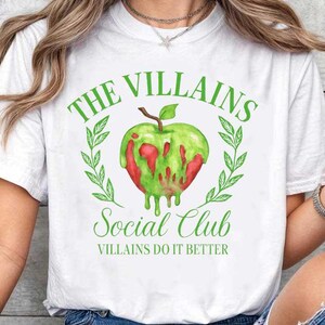May include: White t-shirt with a green and red apple graphic. The text on the shirt reads "THE VILLAINS SOCIAL CLUB" and "VILLAINS DO IT BETTER" in green. The apple design is surrounded by green leaves.