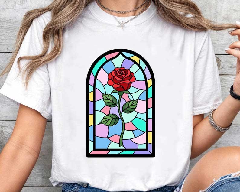 May include: White t-shirt with a stained glass rose design. The graphic shows a red rose with green leaves, within a colourful, arched window frame. The design is centered on the shirt.