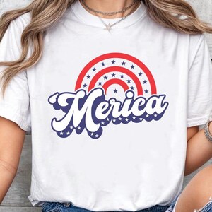 May include: White t-shirt featuring a red, white and blue graphic of a rainbow with stars and the word "Merica" in a retro font.
