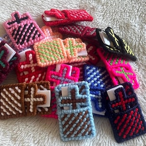 May include: A collection of small, rectangular, hand-stitched yarn pouches in various colors including pink, red, blue, brown, and black. Each pouch features a cross-shaped flap closure and contains a small white paper insert tucked inside.