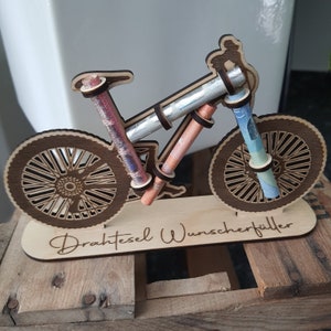 May include: A wooden bicycle money holder with the text "Drahtesel Wunscherschfiller" on the base. The bicycle is decorated with rolled up bills of money.