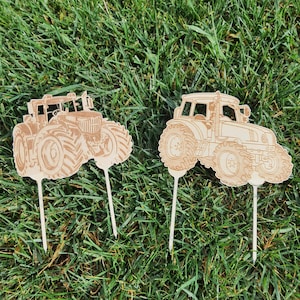 May include: Two wooden tractor cake toppers, one red and one green, with detailed designs. The toppers are perfect for a farm-themed party.