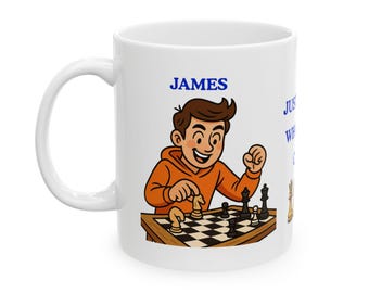 May include: White ceramic mug featuring a cartoon illustration of a person playing chess. The person is wearing an orange hoodie and the name "JAMES" is printed in blue. The mug has a black and white checkered chessboard design.
