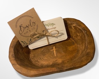 May include: A wooden bowl with a cross design, a small stack of cards with the word "Blessings" printed on them, and a brown paper tag with the text "Bowls by Kim & Co."