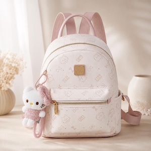 May include: A light pink mini backpack featuring an all-over print of Hello Kitty faces and bows. The bag includes a gold-tone metal logo plaque, a front zipped pocket, and a plush Hello Kitty character keychain attached to the side strap.
