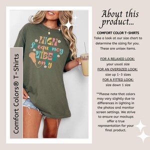 May include: Olive green Comfort Colors t-shirt with the text "HIGH frequency VIBE only" in colorful lettering. The shirt is a unisex item. The image also includes text about sizing and color variations.