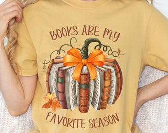 May include: Mustard yellow t-shirt featuring a pumpkin made of books with an orange bow and the text "BOOKS ARE MY FAVORITE SEASON". The pumpkin design has a green stem and autumn leaves.