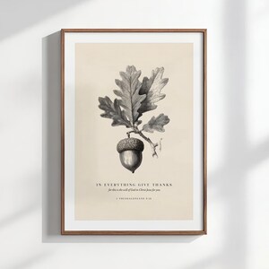 May include: A framed botanical print showing a detailed grayscale illustration of an oak branch with leaves and an acorn. The text reads "IN EVERYTHING GIVE THANKS" with a Bible verse below. The frame is brown.