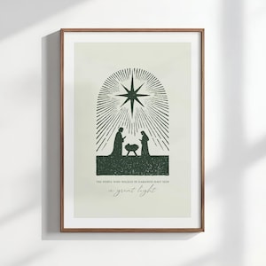 Puede incluir: Una impresión enmarcada con una ilustración verde oscuro de una escena de la Natividad. La imagen incluye siluetas de María, José y el niño Jesús bajo un diseño de estrella. El texto dice: "THE PEOPLE WHO WALKED IN DARKNESS HAVE SEEN a great light."