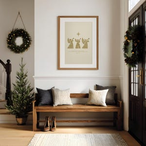 May include: A cozy entryway decorated for the holidays. A framed print with angels hangs above a wooden bench with pillows. A small Christmas tree and wreaths add festive touches. The floor has a rug and a pair of shoes.
