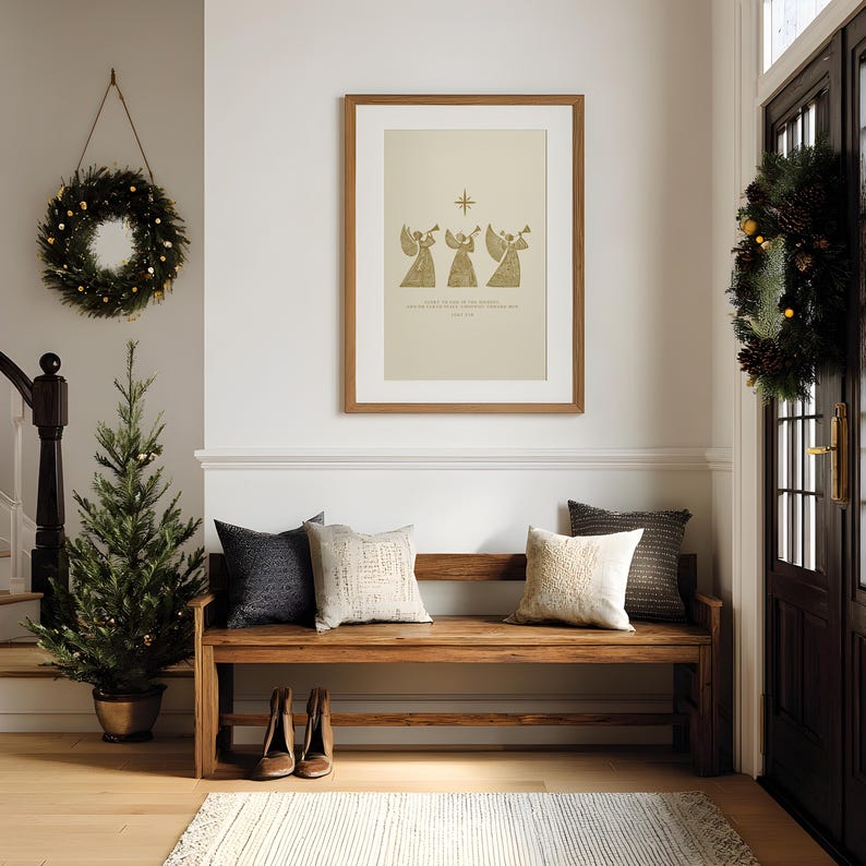 May include: A cozy entryway decorated for the holidays. A framed print with angels hangs above a wooden bench with pillows. A small Christmas tree and wreaths add festive touches. The floor has a rug and a pair of shoes.